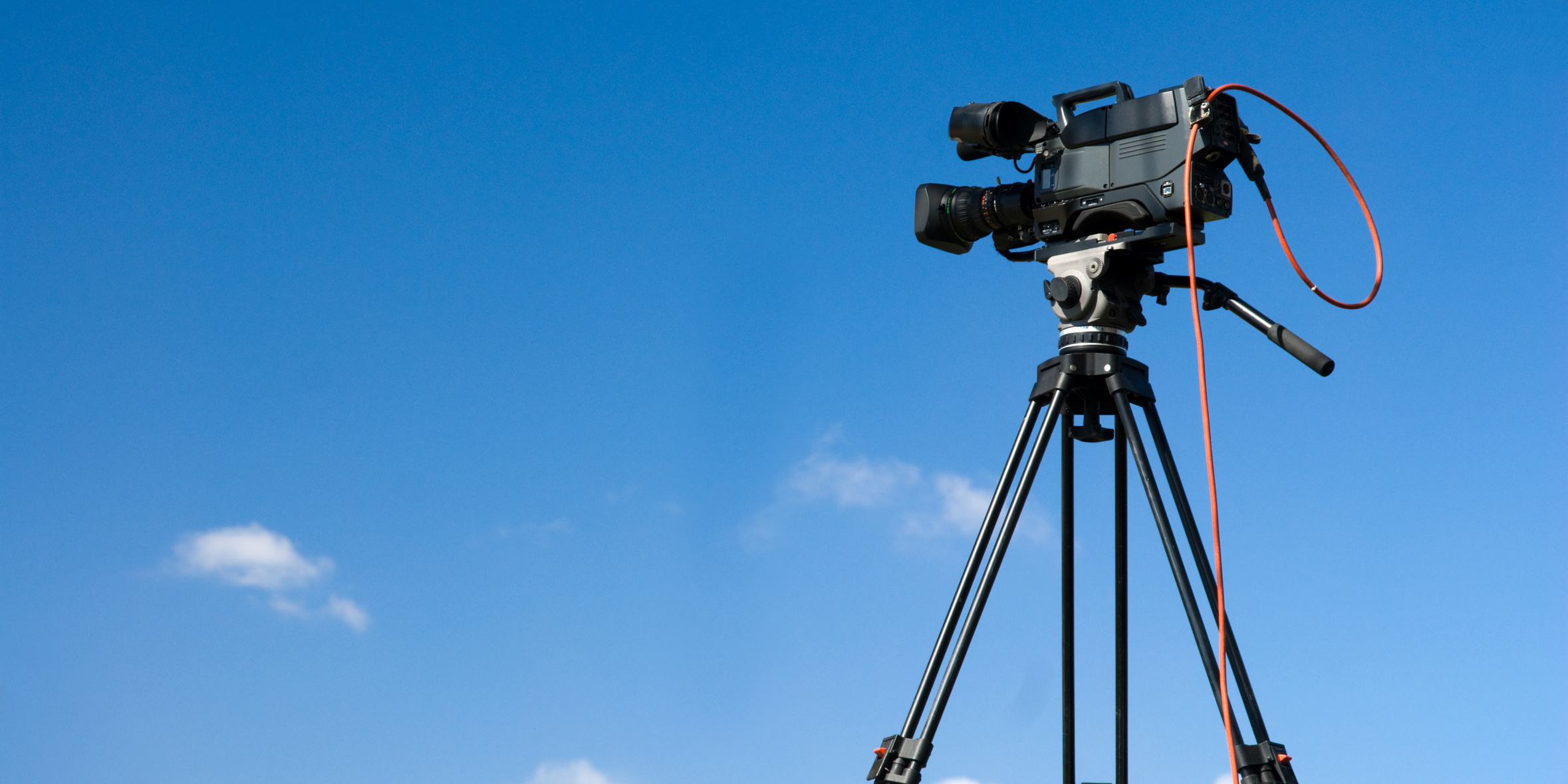 青空をバックに撮影待ちのビデオカメラ